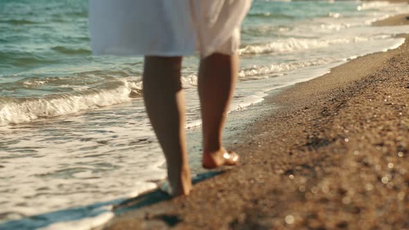 Slim Female Legs and Feet Walking Along Sea Water Waves on Sandy Beach