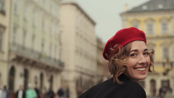 Smiling Young Woman In Red Beret And Red Dress Running Across City Square.