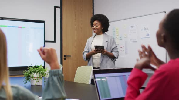 African american businesswoman using tablet presenting to female colleagues at office meeting