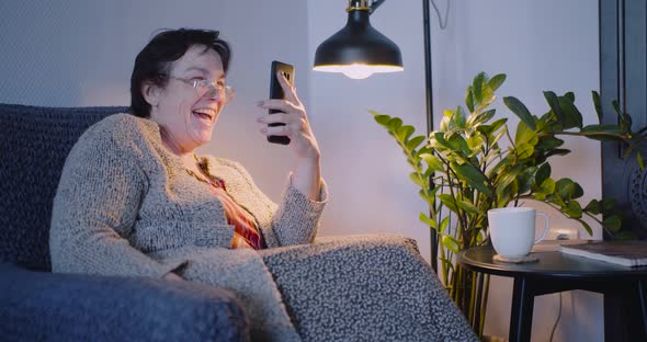 60 Years Old Woman at Home with Smartphone She Receives a Funny Message on Her Smartphone and Laughs