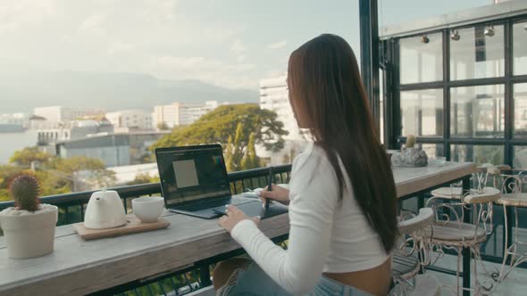 A Young Asian Girl Works at Her Laptop in a Rooftop Cafe in the City