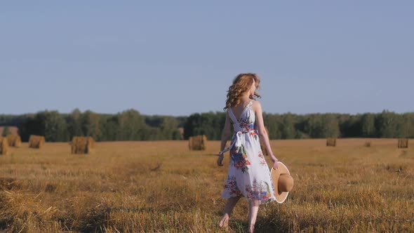 Redhaired Woman in Dress and Hat Cheerfully Walks in the Field
