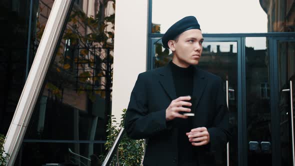 Confident and Handsome Young Businessman with Beret Walking Down Modern City Street and Looking Away