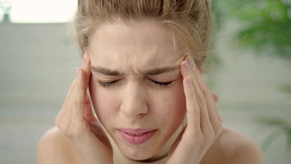 Close Up Young Brunette Woman with Bun on Her Head is Experiencing Severe Headaches