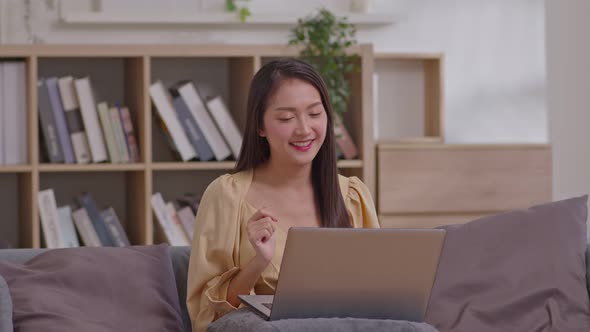 Energetic Asian girl working on laptop from home office. Female executive using computer remote stud