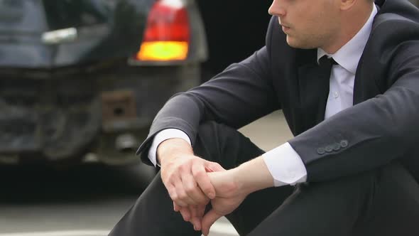 Desperate Man Sitting Asphalt on Crashed Car With Hazard Lights Background