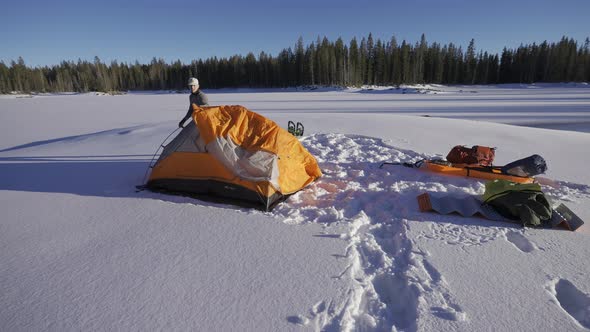 Man setting up an orange tent in the snow while camping.