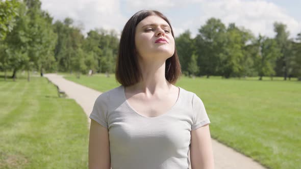 A Young Caucasian Woman Looks Around with a Smile on a Pathway in a Park on a Sunny Day