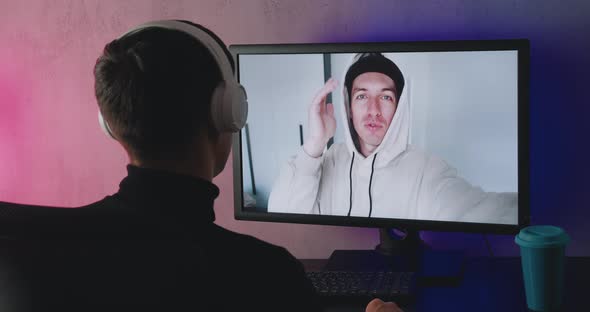 Rear View of a Young Man with Headphones Using Computer for Online Call Conference From Home