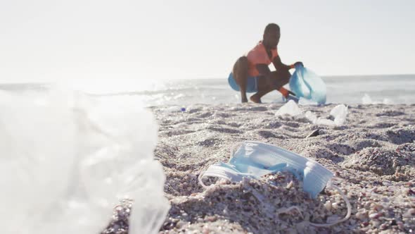 African american man segregating waste with gloves on sunny beach