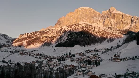 Cinematic descending drone shot of mountain village at the base of a large mountain sunrise light