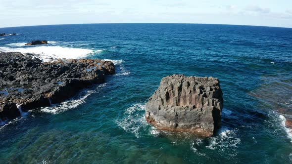 Aerial arc shot around small island of basalt columns in ocean surf