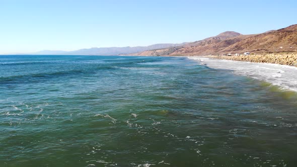 Aerial drone shot over the blue ocean waves and epic California beaches extending into the distance