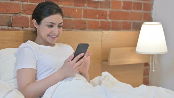 Young Indian Woman using Smartphone in Bed