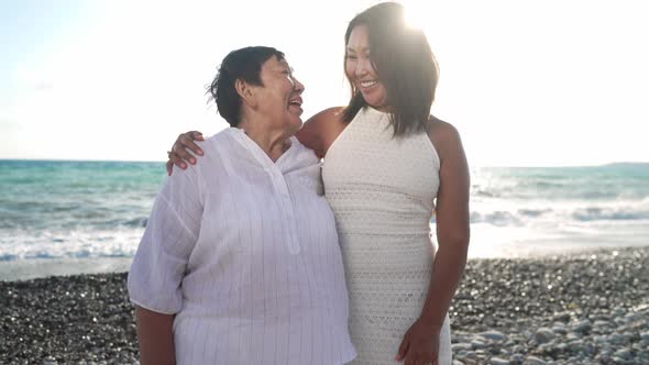 Happy Asian Daughter and Old Mother Talking Standing at Sunset on Picturesque Mediterranean Sea