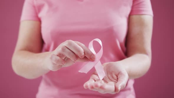 Mid section of woman holding a pink ribbon against pink background