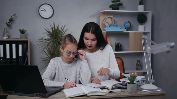 Beautiful Brunette Woman Helping Her Intelligent Teen Daughter in Glasses to do Hometask