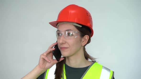 A Beautiful Young Female Construction Worker in a Safety Helmet Smiling on the Phone