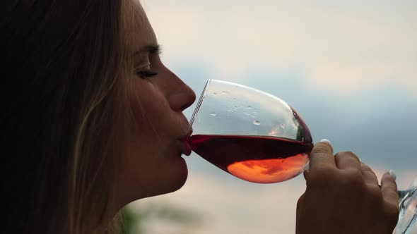 Beautiful Woman Drinks Red Wine From a Glass at Sunset in the Vineyard