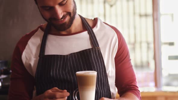 Smiling waiter holding coffee at counter in cafe