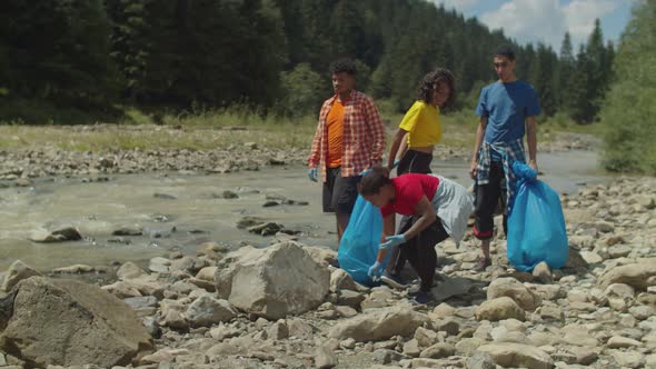 Diverse Multiethnic Environmentalists Carrying Garbage Bags After Cleanup in Mountain Riverbank