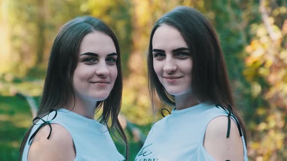 Twins Girls Smiling and Look at Camera in Green Nature Background