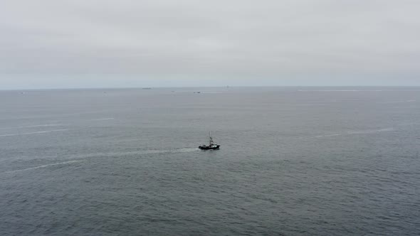 Drone aerial tracking alongside a lone fishing boat going out to see on a cloudy and calm day.