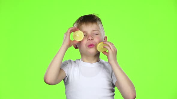 Little Boy with Slices of Lemon Licks Them and Shows Grimaces. Green Screen. Slow Motion