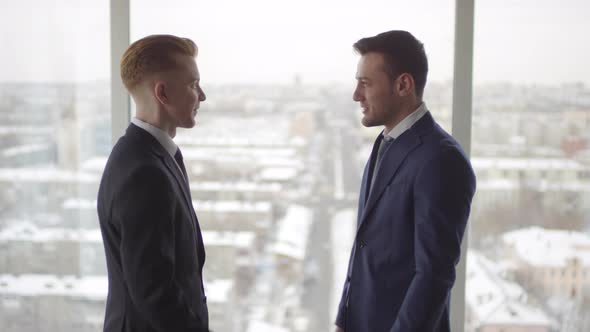 Businessmen in Suits Shaking Hands before Panoramic Window