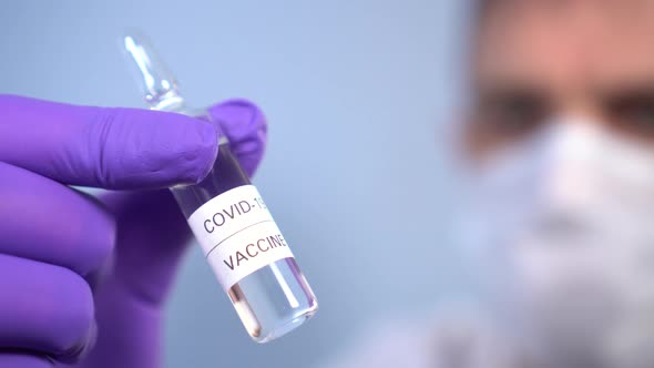 Coronavirus vaccine ampoule in doctor's hands in face mask and protective medical gloves