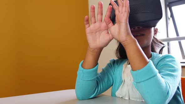 Schoolgirl using virtual reality glasses in classroom at school