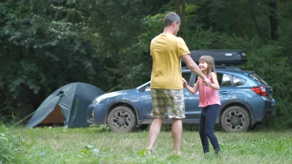 Young father and his child daughter dancing having fun outdoors at camping site in summer.