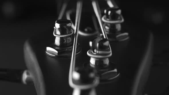 A headstock of a fretless electric bass guitar on the dark background, black and white, closeup