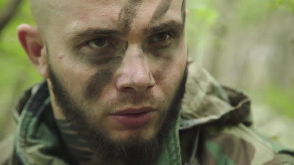 Angry Fighter in Camouflage with Soot Strips on Face Starring in Forest