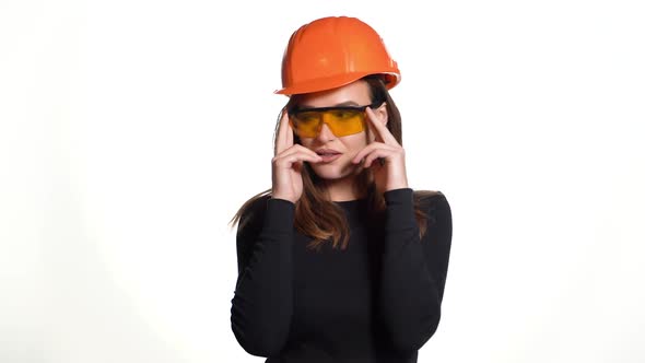 A joyful woman in orange helmet for building is trying on goggles and posing in it