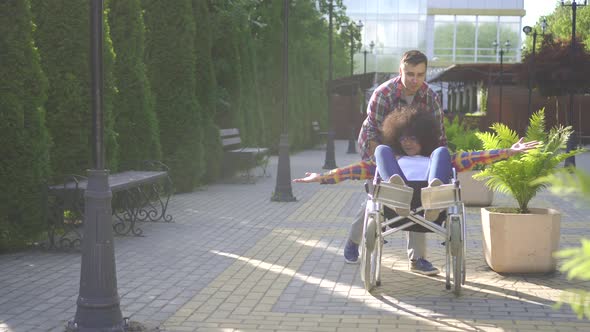 African Woman with an Afro Hairstyle Disabled in a Wheelchair in the Park for a Walk with a Friend