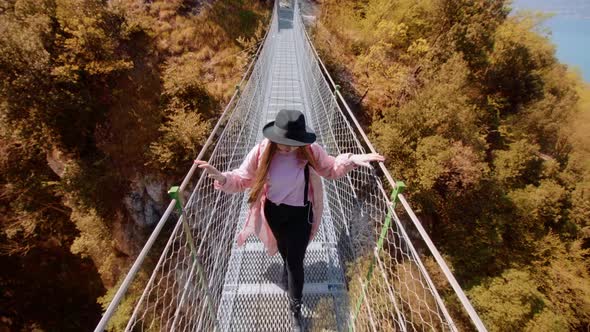 Lady Tourist in Hat Walks on Suspension Bridge Over Gorge