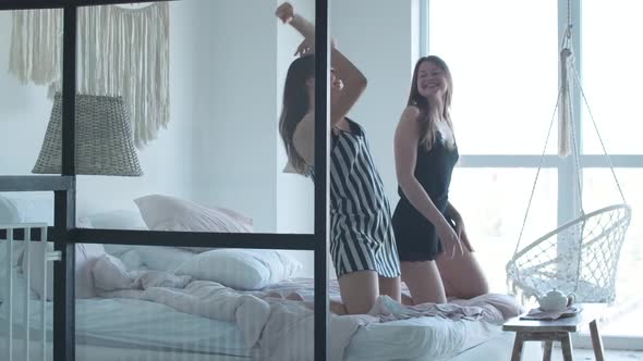 Positive Gay Female Couple Dancing on Bed in the Morning. Portrait of Happy Young Caucasian Lesbians