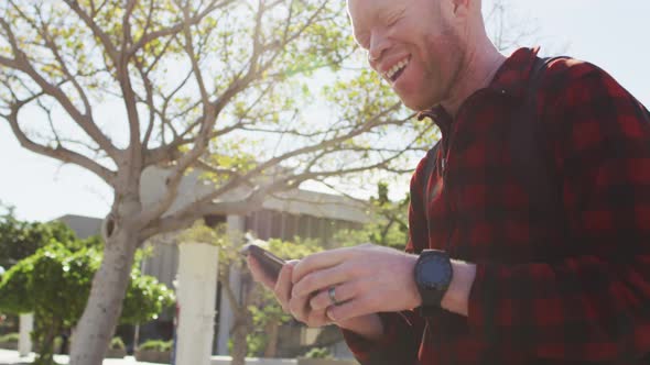 Happy albino african american man with dreadlocks using smartphone