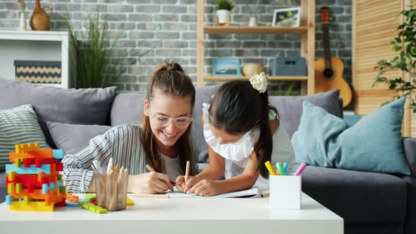 Happy Little Girl Drawing at Home with Caring Mother Using Pencils Having Fun