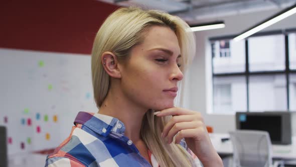 Caucasian businesswoman rubbing her chin in thought and smiling in office