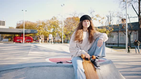 General Shot of a Stylish Young Girl Sitting on a Springboard in a Skatepark and Holding Her