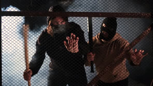 Two Aggressive Masked Men with Baseball Bats are Trying to Break Down the Fences