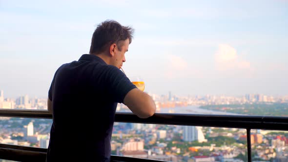 Adult Man Drinking Alcohol Cocktail at Luxury Rooftop Restaurant with Cityscape View at Evening