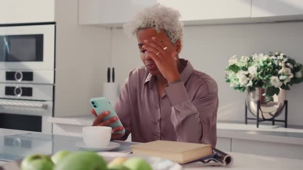 Worried Latina Woman Having Problems with Mobile Phone Sitting in Kitchen