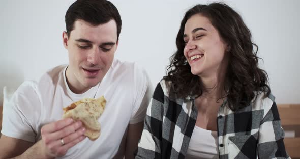 A Happy Couple Man and Woman are Eating Pizza in a Bed at Home