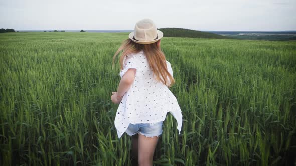 Pretty Child in the Hat Is Running Across the Wheat Field. Happy Young Girl Running in the Field at