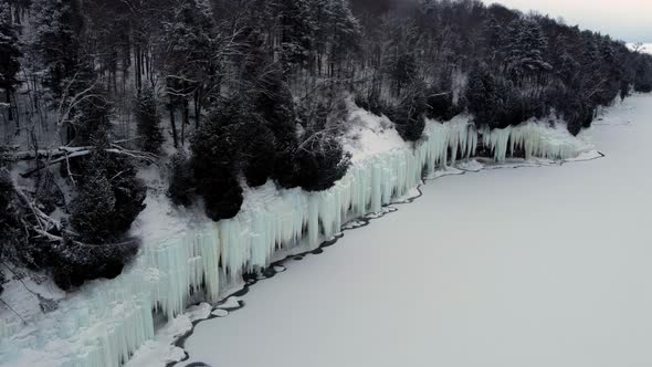 Aerial Flight Over the Cliff Near the Lake From Which Hang Huge Icicles