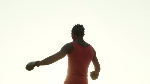 AfricanAmerican Male Athlete Stands on Bright White Background and Raises His Hands in Boxing Gloves