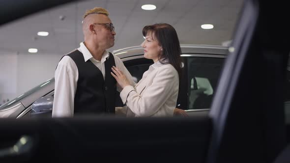 Happy Romantic Husband and Wife Talking Standing in Car Dealership Discussing Purchase